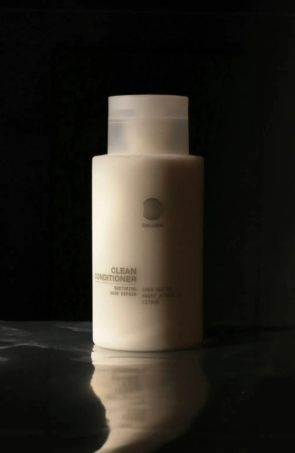 Eine weiße Flasche DALUMA Clean Conditioner steht aufrecht auf einer glänzenden Oberfläche vor einem dunklen Hintergrund, wobei das Produktetikett durch sanfte Beleuchtung hervorgehoben wird.