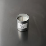 Eine weiße DUFTKERZE GRADE 0.1 RELIEVE von Nullpunkt in einem mattsilbernen Behälter ruht auf einer glatten grauen Oberfläche - ideal für Entspannung und Aromatherapie.