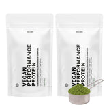 Zwei weiße DALUMA VEGANES PERFORMANCE PROTEIN NEUTRAL DOUBLE-Beutel stehen aufrecht nebeneinander, davor befindet sich eine Metallkugel mit neutralem pflanzlichem Proteinpulver.