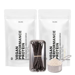 Zwei weiße, wiederverschließbare Beutel mit der Aufschrift VEGANES PERFORMANCE PROTEIN VANILLE DOUBLE von DALUMA stehen hinter einem Metalltablett mit Vanilleschoten und einem mit Vanilleproteinpulver gefüllten Messbecher.