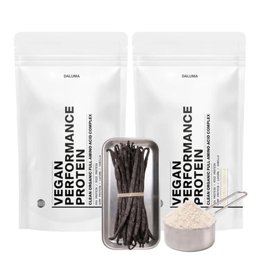 Zwei weiße, wiederverschließbare Beutel mit der Aufschrift VEGANES PERFORMANCE PROTEIN VANILLE DOUBLE von DALUMA stehen hinter einem Metalltablett mit Vanilleschoten und einem mit Vanilleproteinpulver gefüllten Messbecher.