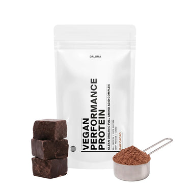 Ein weißer VEGANES PERFORMANCE PROTEIN KAKAO-Beutel von DALUMA steht aufrecht, mit drei gestapelten Schokoladenstückchen und einer Metallkugel mit reichhaltigem Rohkakao-Pulver davor, um die Premium-Qualität hervorzuheben.
