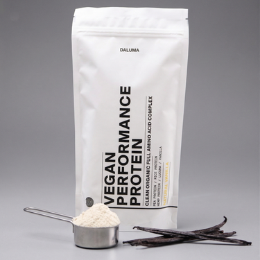 Eine weiße DALUMA VEGANES PERFORMANCE PROTEIN VANILLE Tüte steht aufrecht und zeigt pflanzliches Protein. Auf der Vorderseite sind eine Metallkugel mit veganem Proteinpulver und Vanilleschoten vor einem schlichten grauen Hintergrund zu sehen.