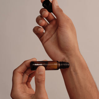 Eine Person hält mit einer Hand eine kleine Braunglas-Rollerflasche mit der Aufschrift Nullpunkt und schraubt mit der anderen Hand den schwarzen Verschluss ab.