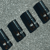 Vier kleine Braunglasflaschen mit schwarzen Deckeln, die mit "0.1", "0.2", "0.3" und "0.4" beschriftet sind, aus dem Nullpunkt NULLPUNKT DISCOVERY SET sind diagonal auf einer gesprenkelten grauen Fläche angeordnet und werfen Schatten nach rechts.