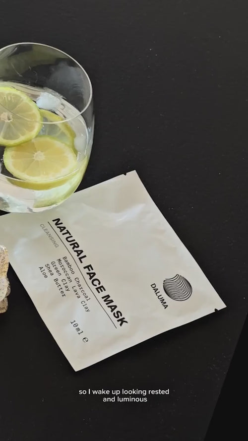 Ein Glas Wasser mit Zitronen- und Limettenscheiben steht neben einer Packung mit der Aufschrift Natural Face Mask auf einer dunklen Fläche. Unten auf der Packung steht: "So wache ich ausgeruht und strahlend auf".