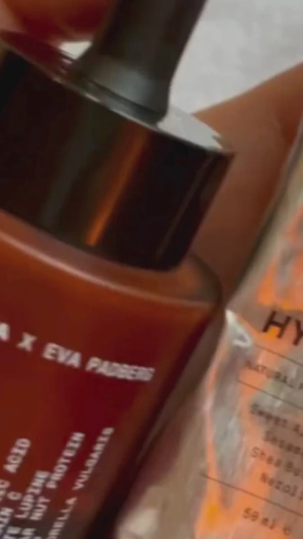 Eine Hand hält eine braune Glastropfflasche mit der Aufschrift Cellular Resurgence Serum neben einer Metalltube mit der Aufschrift Hydrate der Marke Daluma.