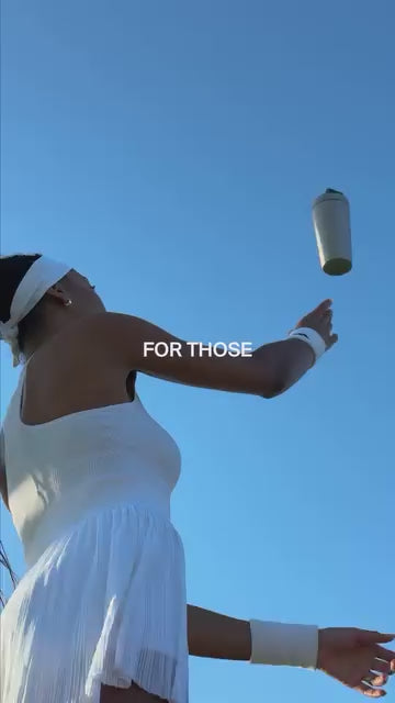Ein Tennisspieler in weißer Sportkleidung und mit Stirnband wirft eine Wasserflasche in die Luft vor einem klaren blauen Himmel. Der Text FOR THOSE erscheint in der Mitte des Bildes.