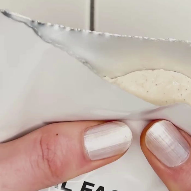 Eine Hand mit weiß lackierten Nägeln hält eine teilweise geöffnete weiße Packung dailumade.comEP HYDRATION FEUCHTIGKEITSMASKE, in der eine cremefarbene beigefarbene Maske zum Vorschein kommt.